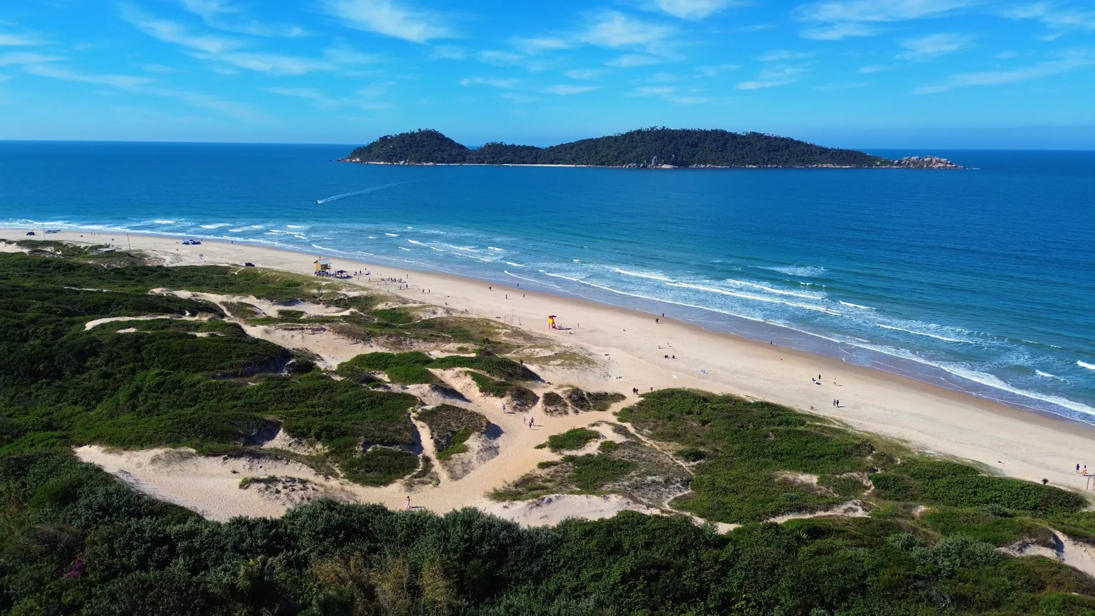 Praia extensa com dunas e ilha no horizonte